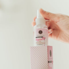 Rose water bottle in hand, clear bottle with pink label, and patterned box with Skalli Essentials branding