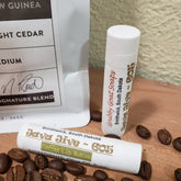 Lip balm tubes with white and gold text, coffee beans on wood surface, Grubby Goat Soaps brand