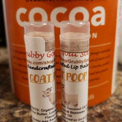 Lip balm tubes with white labels, clear caps, and "GOAT POOP" text, with orange cocoa container background
