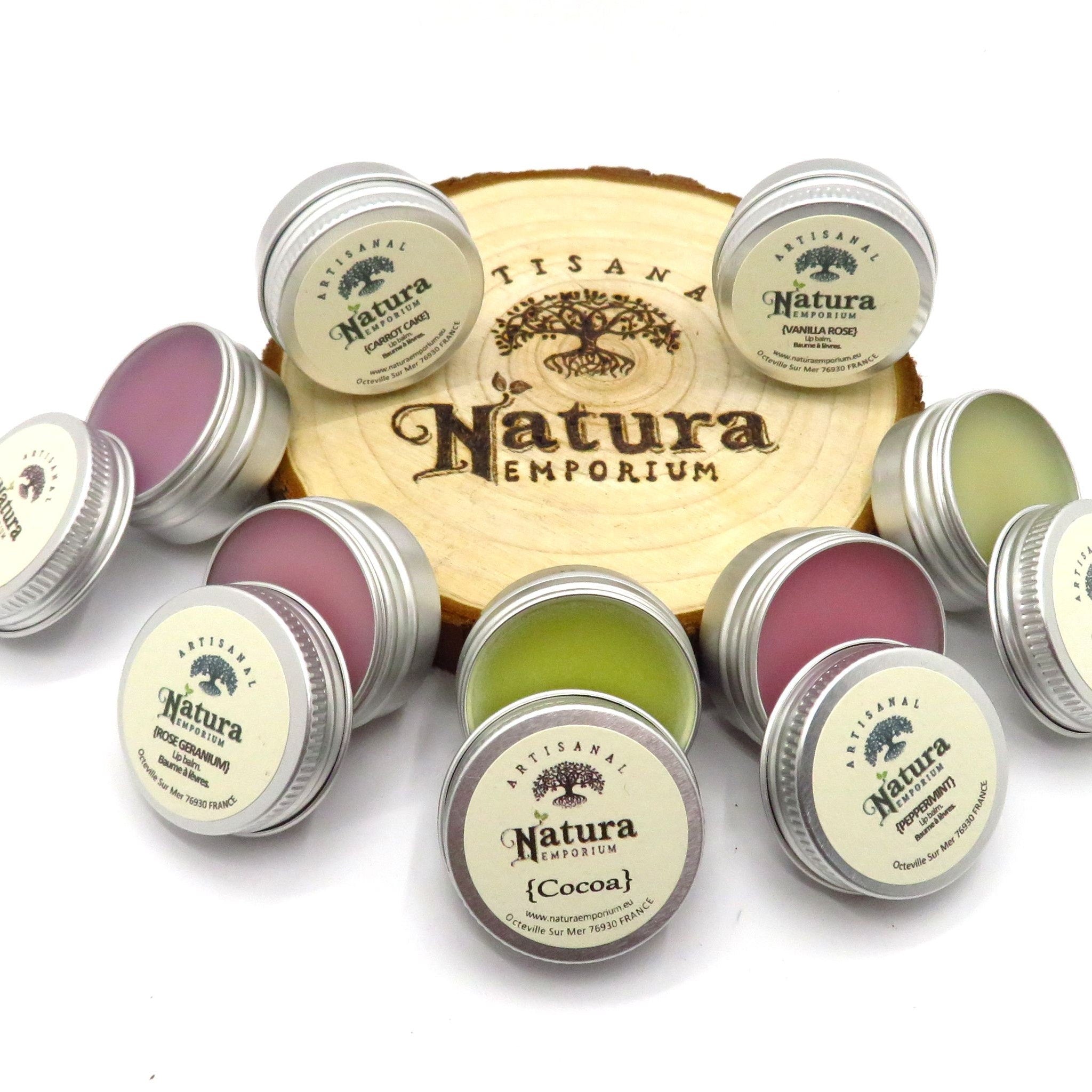 Lip balm tins with Natura Emporium labels, silver metal, various colors, on wood slice