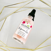 Facial cleanser bottle, pink liquid, black pump, Delizioso Skincare label, rose design on a mirrored surface