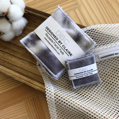 Reusable facial pads with gray tie-dye pattern, white stitching, and DBC Designed By Claire branding in mesh bag