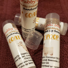 Lip balms white tubes with goat graphic and GrubbyGoatSoap text, clear cap on red fabric