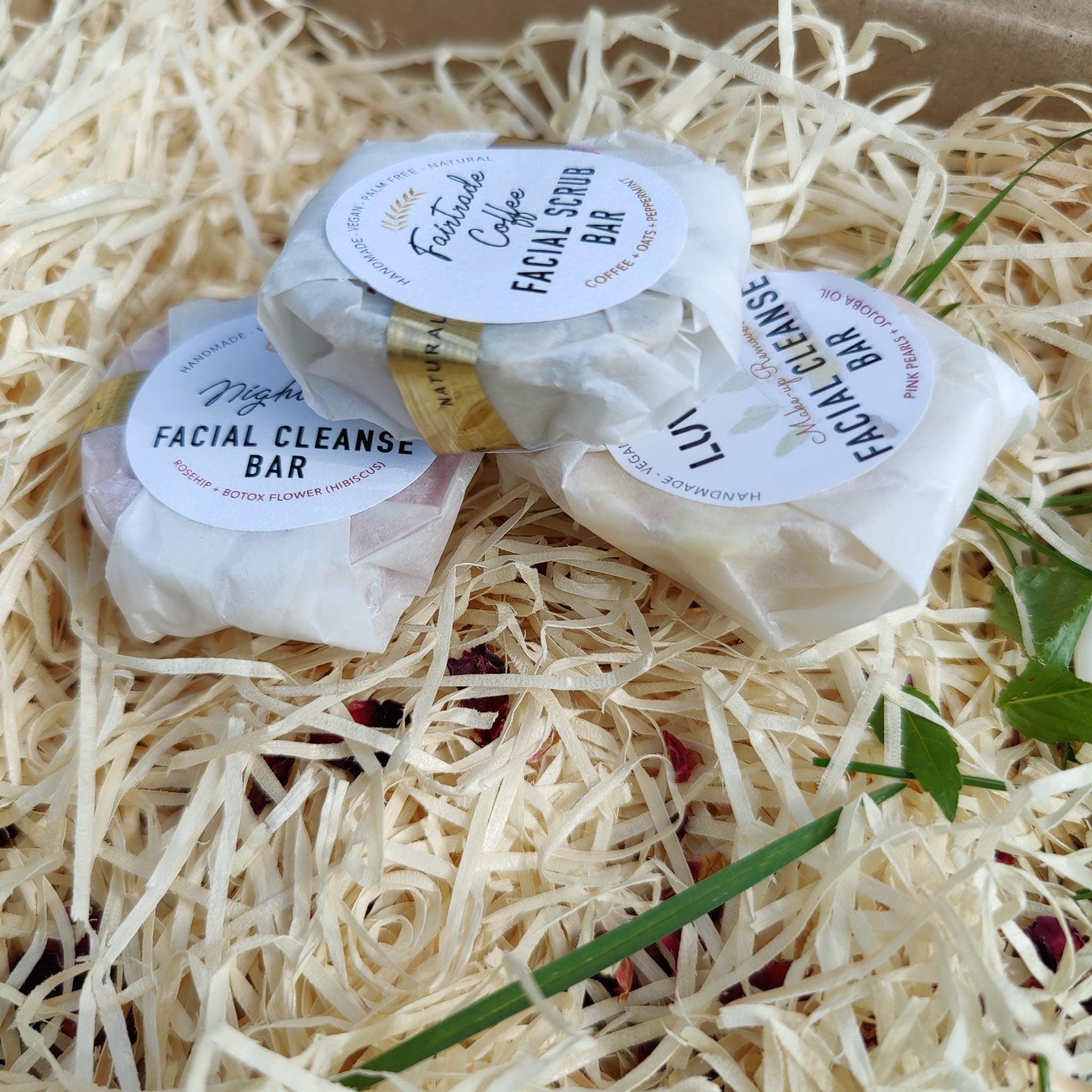 Facial cleanser bars wrapped in white paper, with Luvyi and other labels, in wood shavings