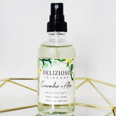 Cucumber toner in clear glass bottle with black spray top, Delizioso Skincare label, and gold geometric stand