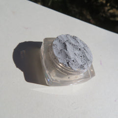 Side view of matte gray loose pigment eyeshadow in minimalist jar with eco-friendly label, showcasing fine powder texture