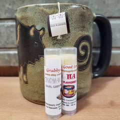 Lip balm tubes with white labels, clear caps, and a mug in background with tea bag