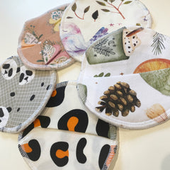 Reusable nursing pads in various patterns and colors, white stitched edges, floral, panda, and leopard print designs