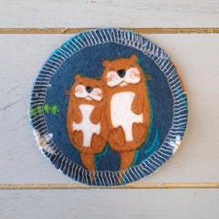 Round blue fabric coaster with otter illustration, brown and white pattern, stitched edge