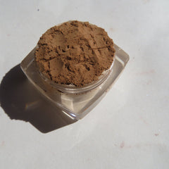 Brown powder in clear plastic container, on white surface with shadow
