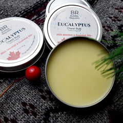 Eucalyptus chest rub in silver tin, yellow balm, and gray knit fabric with red accents