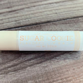 Sugar cookie lip balm tube, off-white and peach text on white label, on wood background