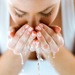 Skincare routine: woman with closed eyes, hands cupping water, clear liquid pouring down