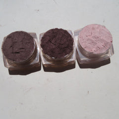 Side view of three matte loose mineral eyeshadows in glass jars with black lids, showcasing rich pigment textures.