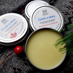 Foot balm in silver tin with yellow balm, "Have A Sole" text, and gray knitted background