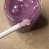Lip gloss with pink glitter on applicator, purple gloss in jar, white wand