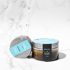 Facial scrub jars with brown contents, gray lids, and blue labels with Manifest Beauty text, water pouring