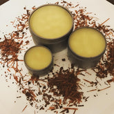 Salve product with yellow salve in metal tins and brown wood shavings on white surface