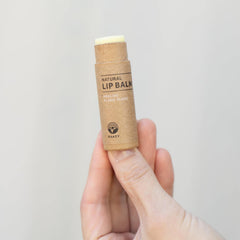 Lip balm tube in brown paper, white balm, held in hand, KAAZY brand visible
