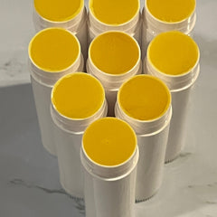 Yellow balm sticks with white containers, arranged in a group on a light surface.