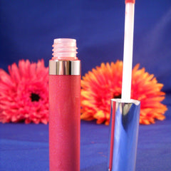 Lip gloss tube coral pink with silver trim and applicator, flowers in background