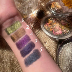 Eyeshadow swatches on wrist, metallic green, brown, purple, and blue shades, makeup application example