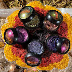 Eyeshadow pots with metallic shimmer in purple, gold, and bronze, with LOVECHILD branding on black lids