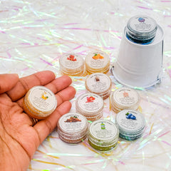 Lip scrubs in clear jars with various colors and labels, held in hand