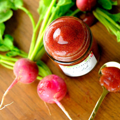 Radish jam in a glass jar, red and speckled, with radishes and green leaves on wood surface