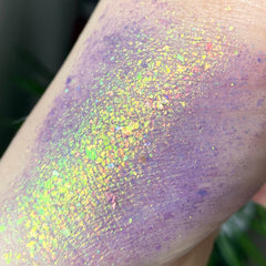 Purple glitter eyeshadow swatch with iridescent flakes on skin, close-up view