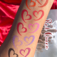 Heart-shaped lip swatches in various colors on arm, with "Red Queen" text visible in background
