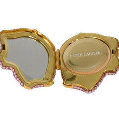 Compact mirror with gold frame, pink gem accents, and Estee Lauder text visible