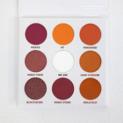 Close-up of a makeup brush applying shimmering maroon eye shadow from the Virginia Tech palette