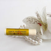 Lip balm tube with yellow label, white flower, and pearl necklace on white surface