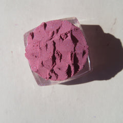 Close-up of loose mineral eyeshadow in pale pink shimmer, showcasing fine sparkle texture and vegan formula