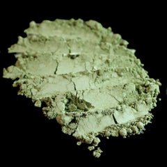 Side view of matte sage green loose mineral eyeshadow in glass jar with gold lid, showcasing powdery texture
