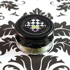 Side view of matte sage green loose mineral eyeshadow in glass jar with gold lid, showcasing olive undertones