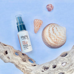 Deep Gel Cleanser bottle, white and black with "shunly" text, next to seashells and driftwood on blue background