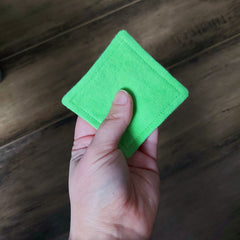 Green square felt coaster held in hand, with stitched edges and wood background