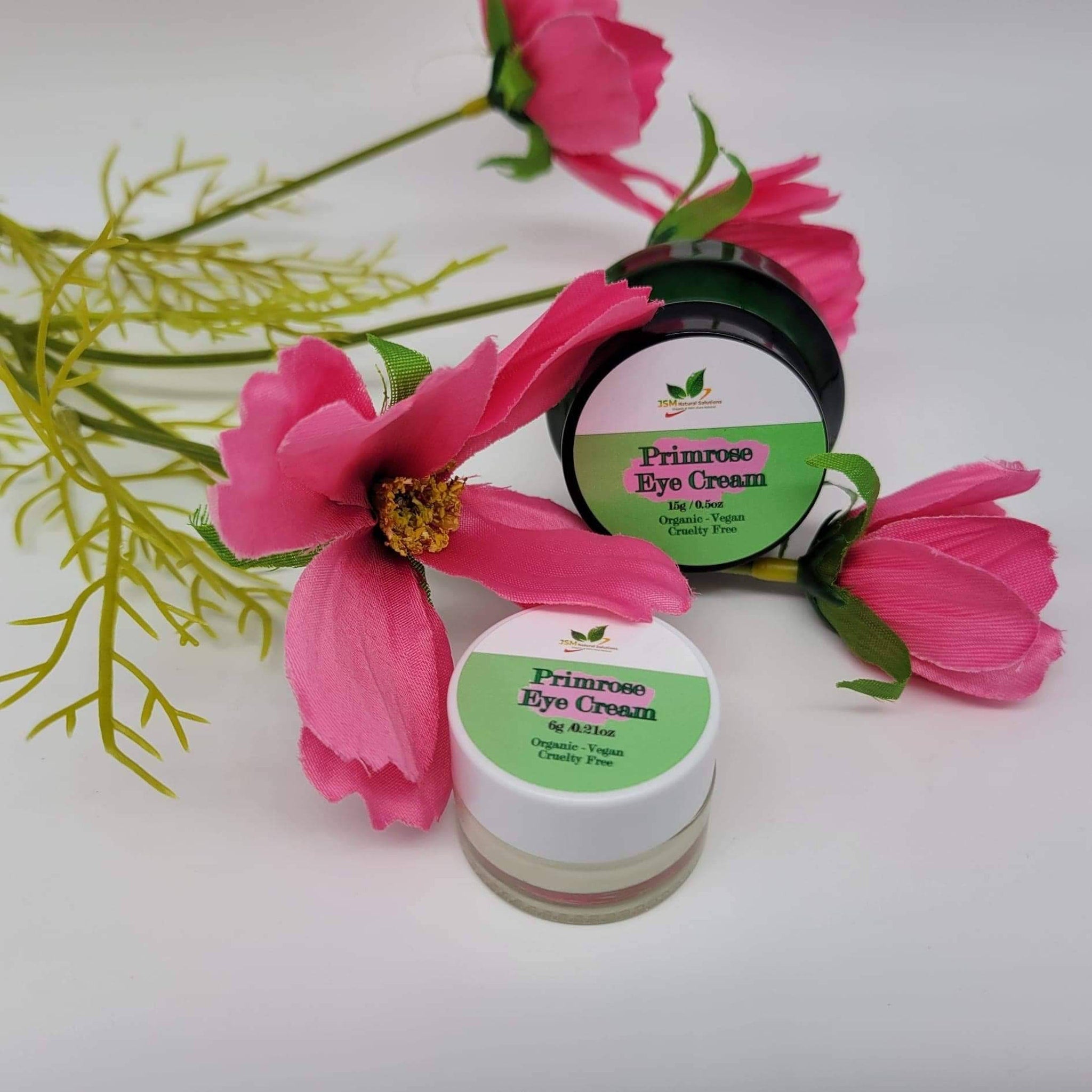 Eye cream jars with white and green labels, pink flowers and green leaves on white background