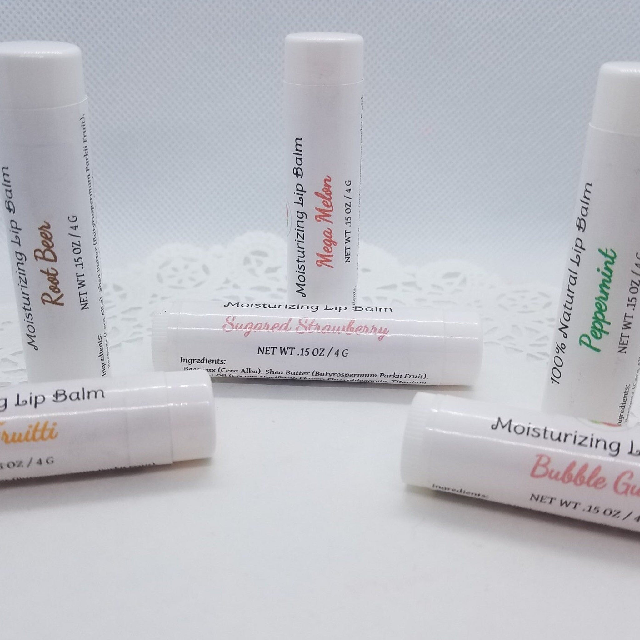 Lip balm tubes, white with various flavor labels, arranged on white surface