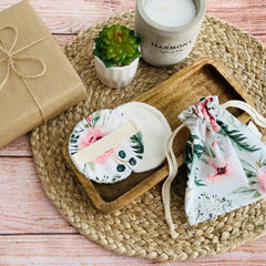 Reusable makeup remover pads with floral print, white fabric, and drawstring bag on woven mat
