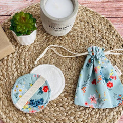 Reusable makeup pads with floral pattern, white fabric, and drawstring bag on woven mat