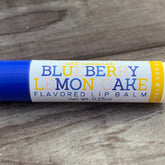 Lip balm tube with blue, white, and yellow text, "Blueberry Lemon Cake" flavor, on wood surface