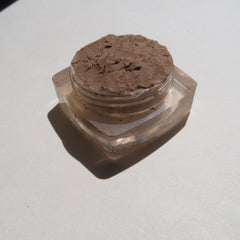 Brown powder in a clear square jar with a light background and shadow