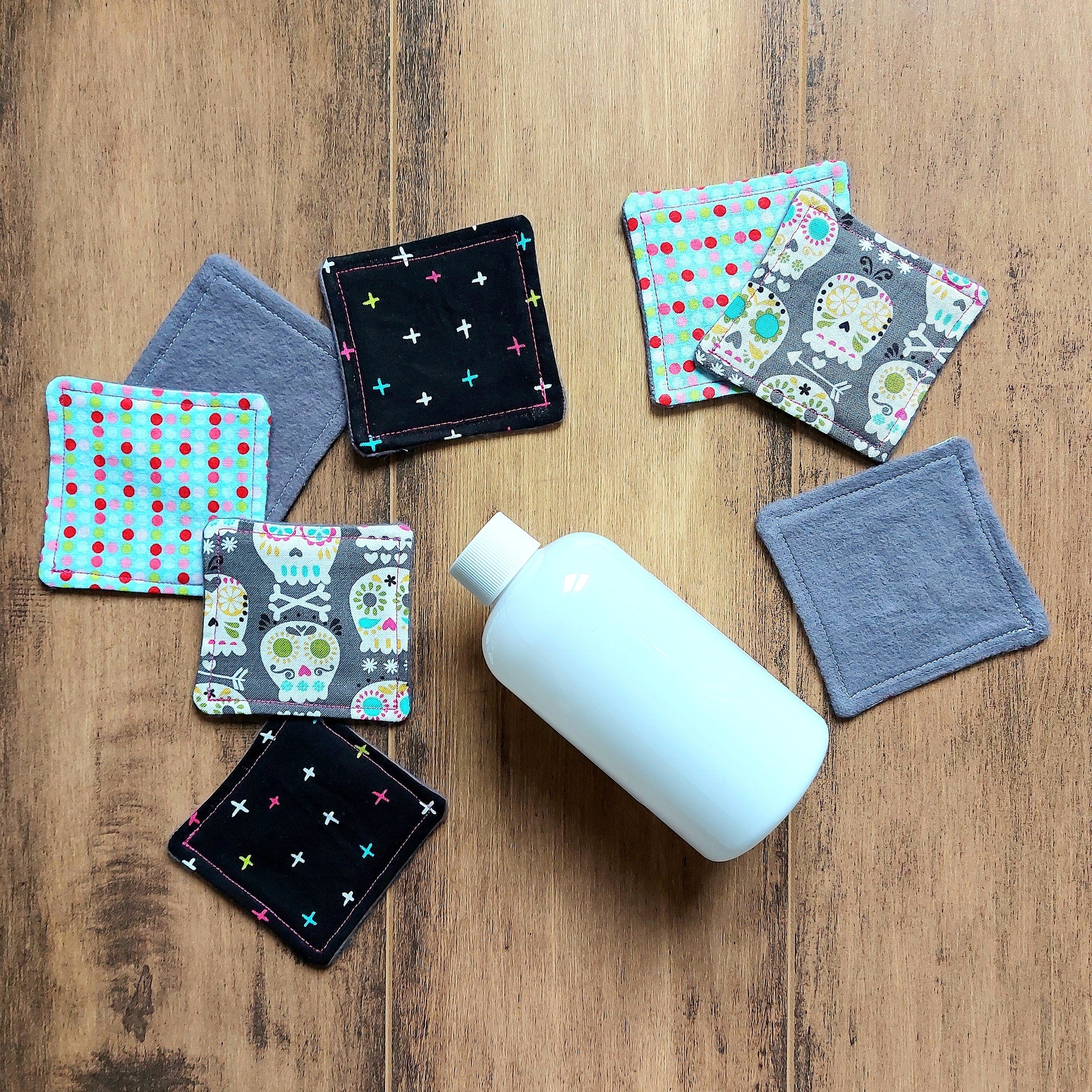 Makeup remover pads with skull, dot, and cross patterns, various colors, and gray fabric on wood surface