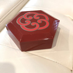 Red hexagonal box with scroll pattern and glossy finish on white surface