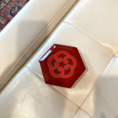Red hexagonal tray with red and gray swirl pattern, resting on white leather cushion