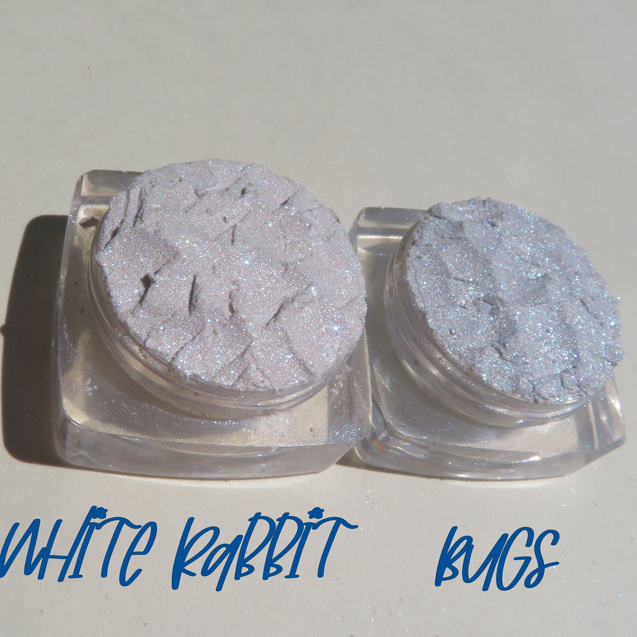Two small jars of loose glitter eyeshadow in shimmering white and soft pink with gold flecks, cruelty-free mineral makeup