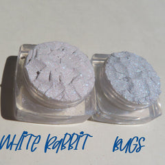 Two small jars of loose glitter eyeshadow in shimmering white and soft pink with gold flecks, cruelty-free mineral makeup